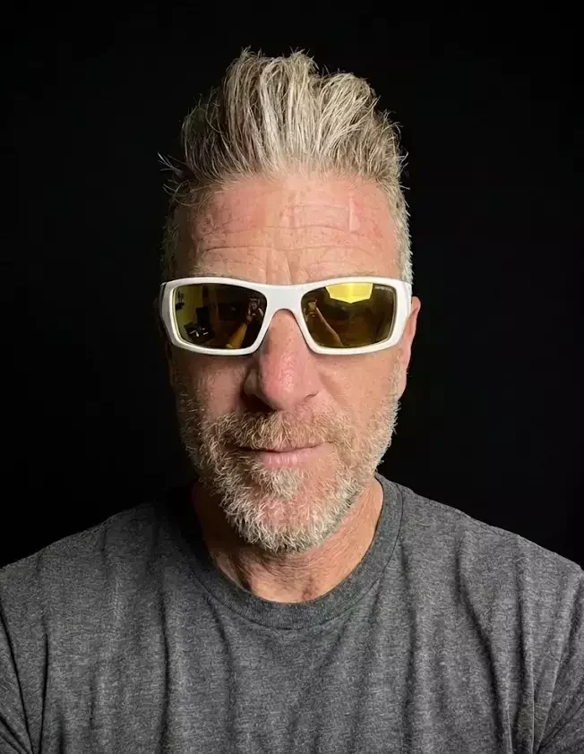 Adam Dailey, founder of Bronco Surf Capital, in white sunglasses with gold lenses against a black background.
