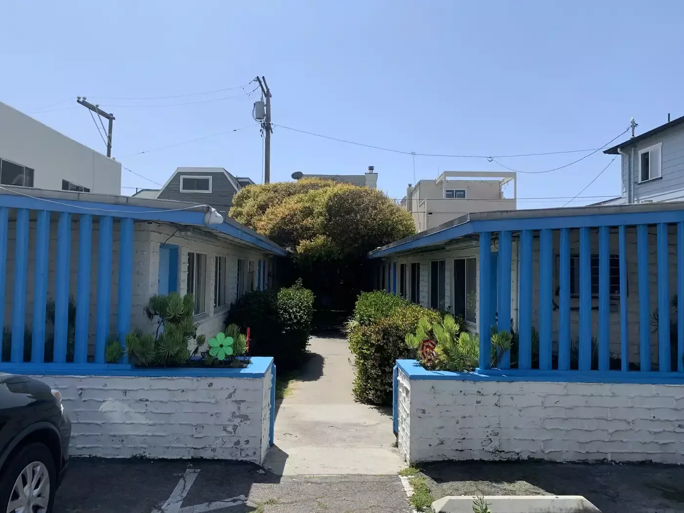 Before: the motel's entry walkway between blue wooden rails and overgrown shrubs.