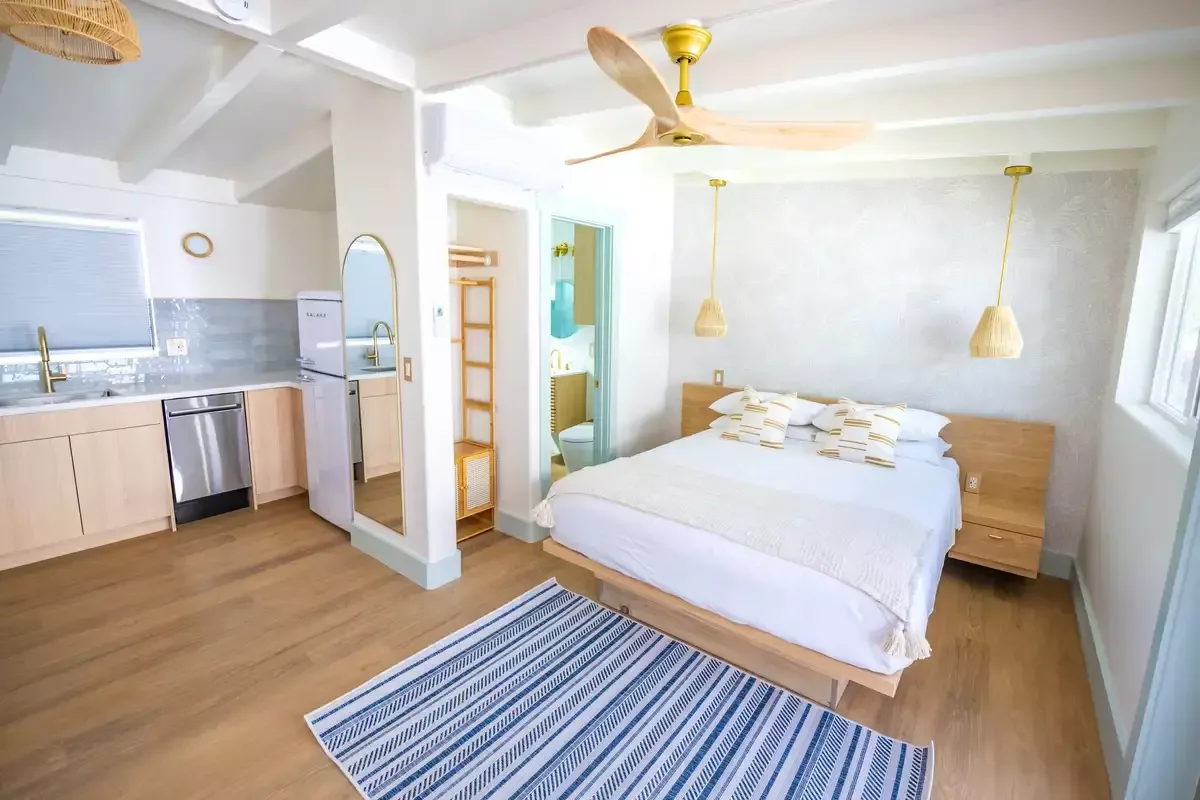 After: a bright remodeled room with a platform bed, wood floors, a striped rug and a kitchenette.