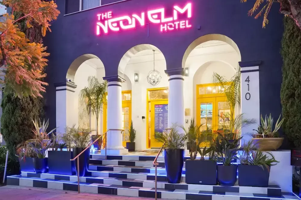 The Neon Elm entry at dusk: three lit arches, checkered steps and the pink neon sign.